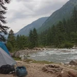 Riverside camping tents in Kasol along Parvati Valley river with pine trees and mountains in Himachal Pradesh India