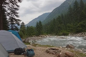 Riverside camping tents in Kasol along Parvati Valley river with pine trees and mountains in Himachal Pradesh India