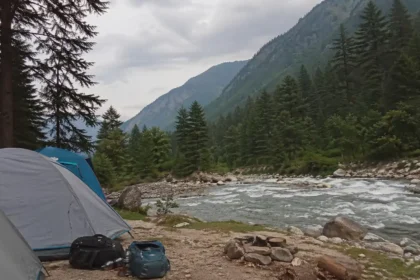 Riverside camping tents in Kasol along Parvati Valley river with pine trees and mountains in Himachal Pradesh India