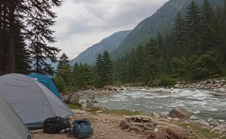 Riverside camping tents in Kasol along Parvati Valley river with pine trees and mountains in Himachal Pradesh India